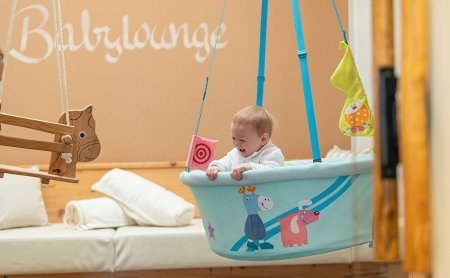 Baby schaukelt fröhlich in bunter Hängeschale in der Babylounge