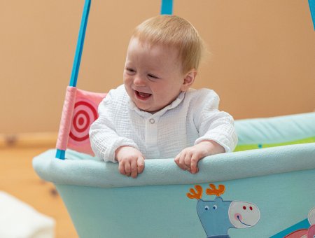 Baby lacht fröhlich in hellblauer Hängeschale mit Tiermotiven