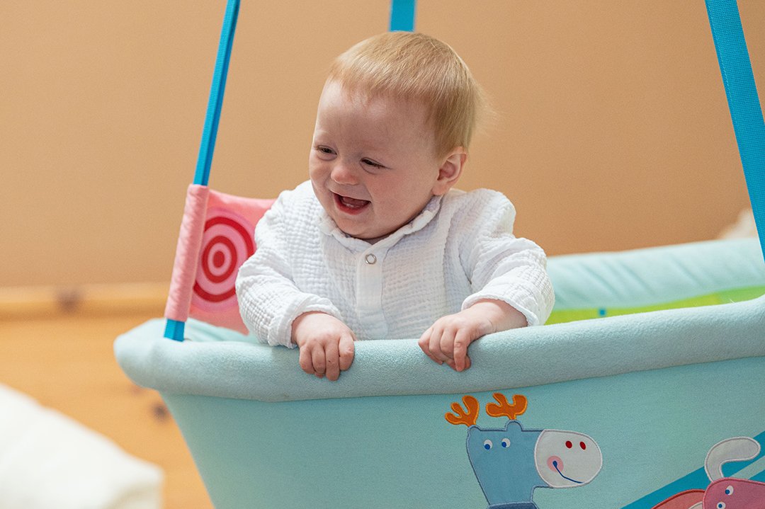 Baby lacht fröhlich in hellblauer Hängeschale mit Tiermotiven