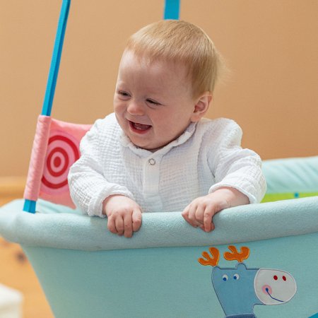 Baby lacht fröhlich in hellblauer Hängeschale mit Tiermotiven