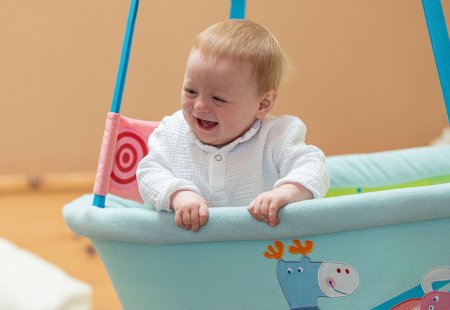 Baby lacht fröhlich in hellblauer Hängeschale mit Tiermotiven