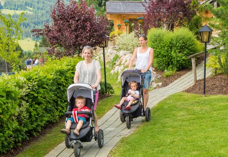 Zwei Frauen spazieren mit Kinderwägen durch den Garten
