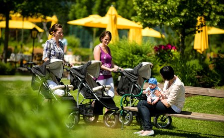 Mütter mit Kinderwägen im sonnigen Garten mit gelben Sonnenschirmen