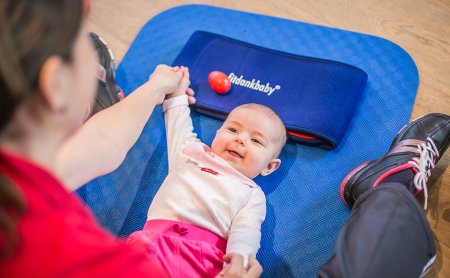 Baby beim Fitdankbaby-Kurs auf einer blauen Matte zwischen den Eltern