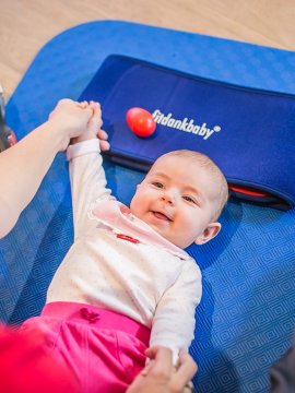 Baby beim Fitdankbaby-Kurs auf einer blauen Matte zwischen den Eltern