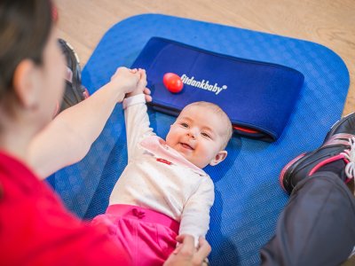 Baby beim Fitdankbaby-Kurs auf einer blauen Matte zwischen den Eltern