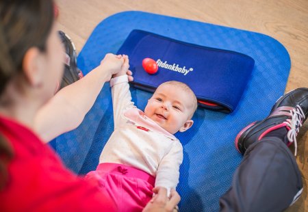 Baby beim Fitdankbaby-Kurs auf einer blauen Matte zwischen den Eltern
