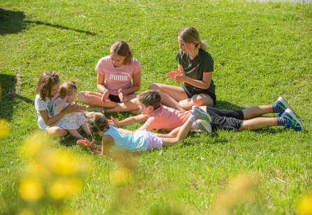 Kindergruppe spielt fröhlich im Gras bei Sonnenschein