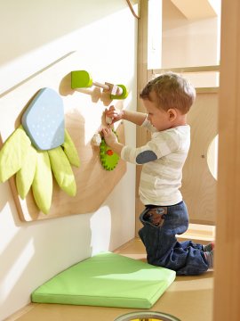 Ein Kleinkind spielt mit einem interaktiven Holzspielzeug an der Wand.