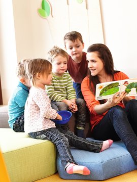 Erzieherin liest mit Kindern ein Bilderbuch in einem hellen Spielraum.