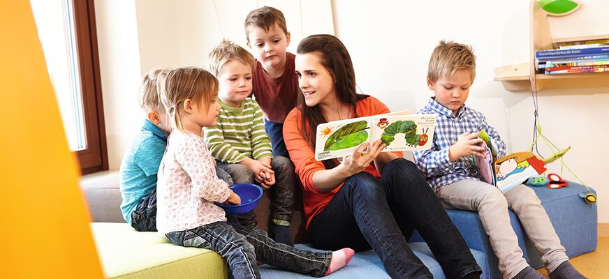 Kindbetreuerinnen liest Kindern aus einem Buch vor