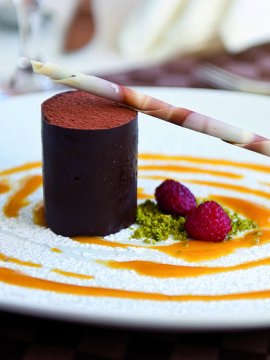 Schokoladen-Dessert mit Fruchtsauce, Beeren, Pistazien und Dekostreifen.
