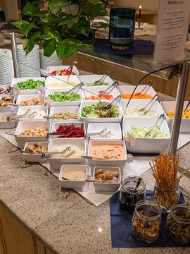 Salad buffet with various bowls of vegetables, greens, and toppings.