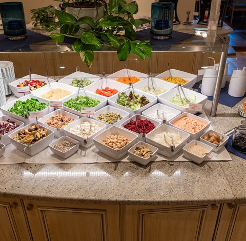 Verschiedene Salatzutaten und Toppings auf einem Buffet, mit Schalen und Zangen.