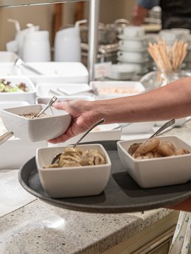 Frau serviert Salate und Beilagen vom Buffet auf einem Tablett.