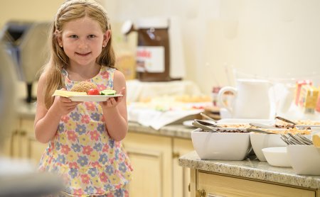 Girl holding plate with sandwich, tomato, and cucumber in kitchen buffet setting