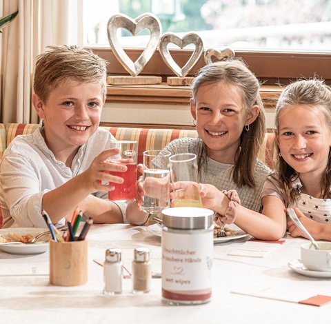 Drei Kinder stoßen mit Getränken an und genießen ihre Mahlzeit.