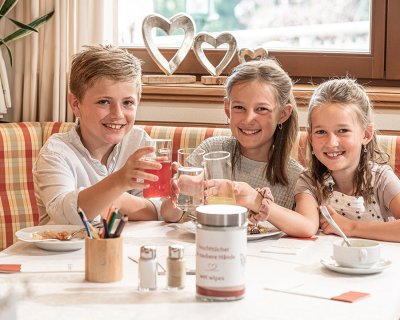 Drei Kinder stoßen mit Getränken an und genießen ihre Mahlzeit.