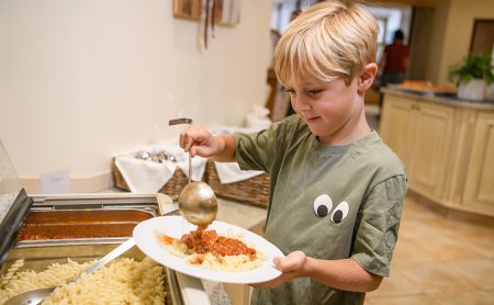 Junge schöpft Tomatensauce auf Pasta auf einem Buffet in einer Küche