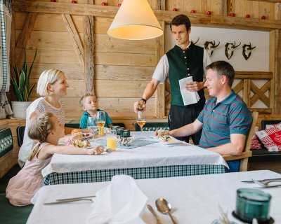 Ein Kellner serviert einem Vater das Essen, während seine Familie am Tisch sitzt.