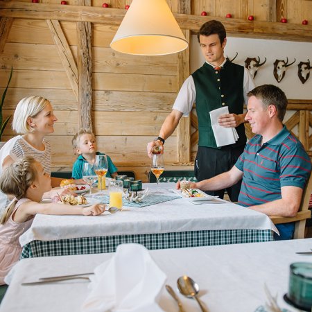Ein Kellner serviert einem Vater das Essen, während seine Familie am Tisch sitzt.