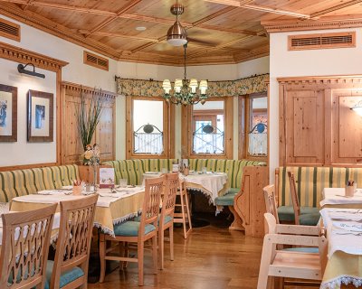 Gemütlicher Restaurantbereich mit grünen Bänken, Holzstühlen, gelb-weißen Tischdecken und dezenten Wanddekorationen.
