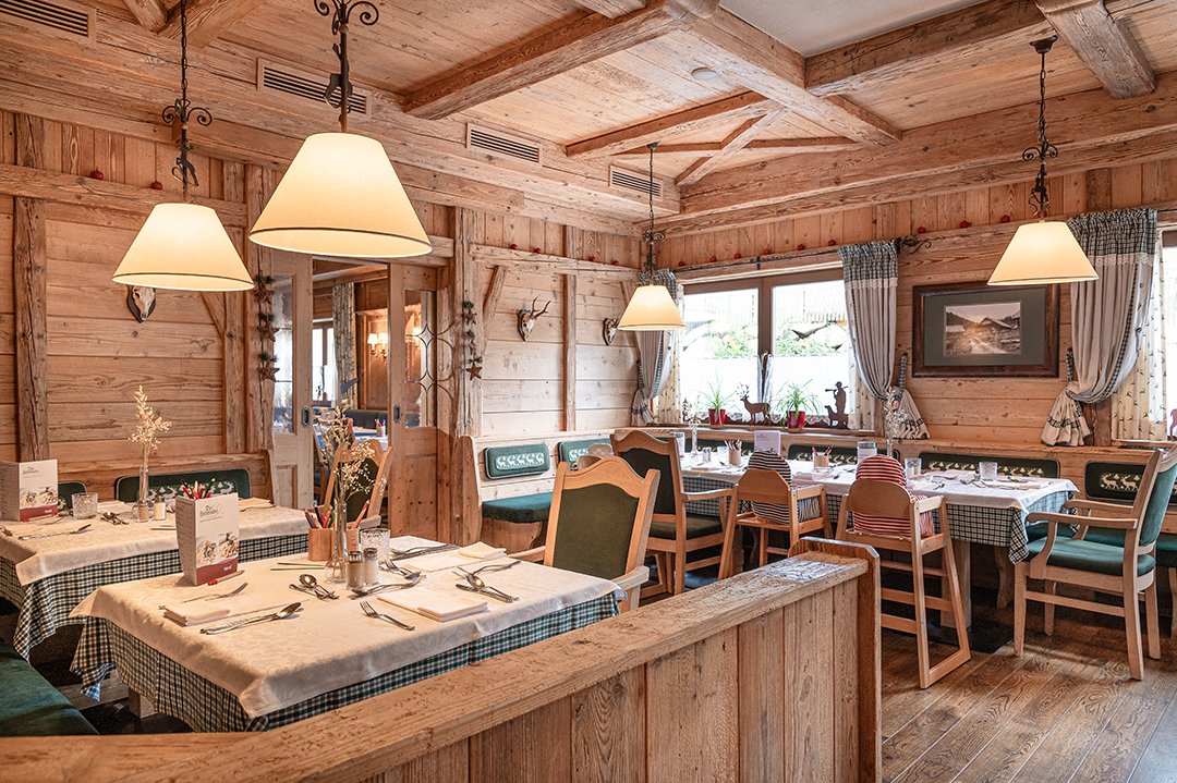 Holzrestaurant mit rustikalem Charme, gedeckte Tische, grüne Bänke und Fensterplatz.
