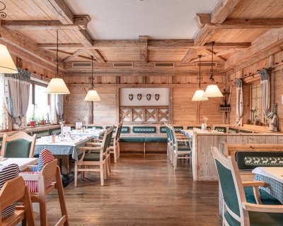 Rustikales Restaurant mit Holzmöbeln, gedeckten Tischen, grünen Bänken und Hirschkopf-Dekor.