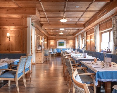 Rustikales Restaurant mit Holzmöbeln, grünen Bänken, gedeckten Tischen und Hirschkopf-Dekor.
