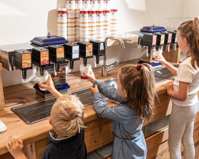 Kinder zapfen Getränke an einem Getränkespender mit verschiedenen Saftsorten.