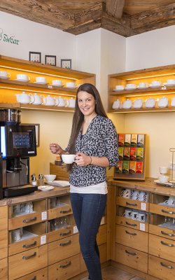 Frau an einer Kaffee- und Teebar, die eine Tasse in der Hand hält, umgeben von Tassen, Tees und Kaffeemaschine.