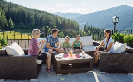 Familie sitzt entspannt auf einer Terrasse mit Bergblick und genießt Getränke.