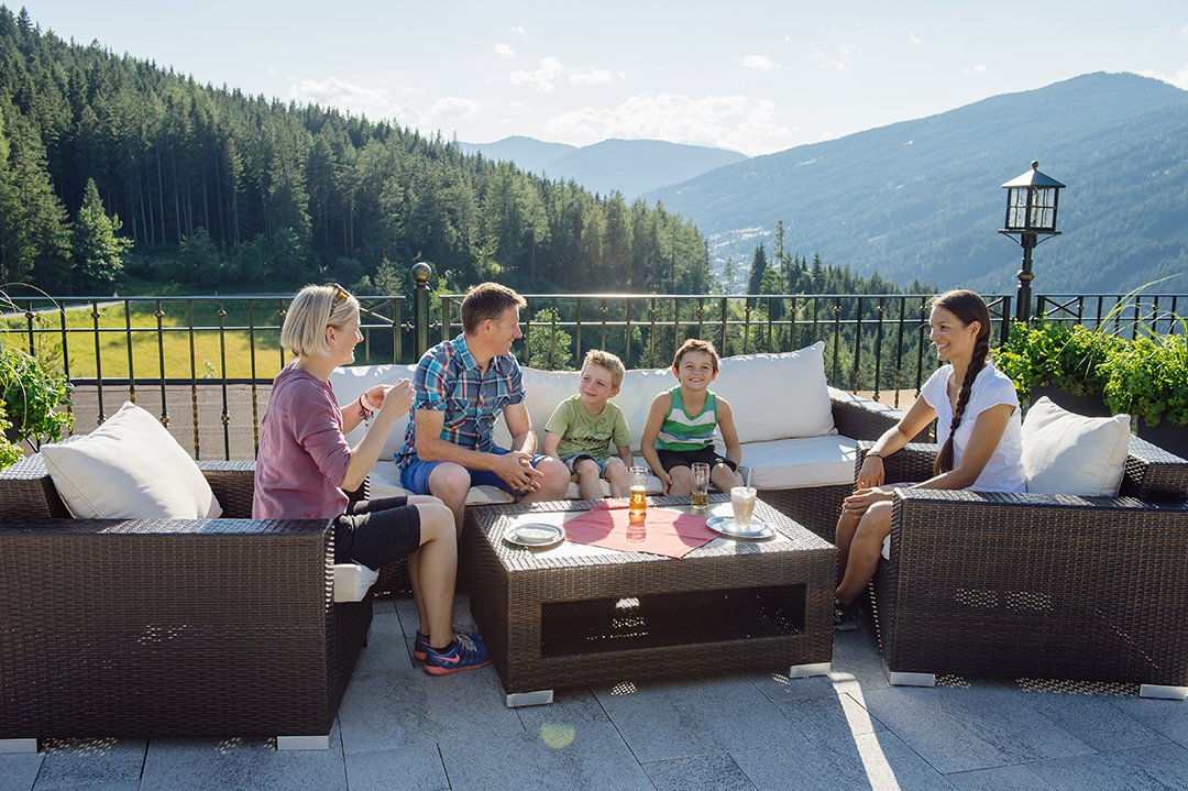 Familie sitzt entspannt auf einer Terrasse mit Bergblick und genießt Getränke.