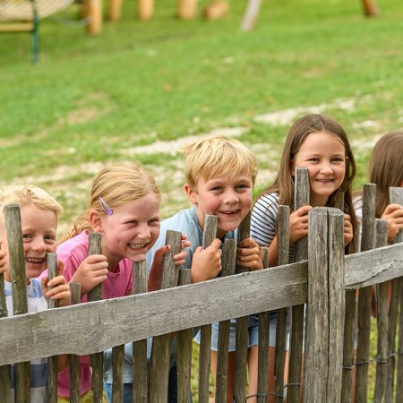 Fünf lachende Kinder lehnen sich hinter einem Holzzaun im Freien