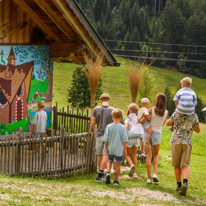 Kindergruppe geht zu einem Holzhaus mit buntem Märchenwandbild in ländlicher Umgebung