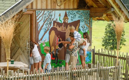 Children looking at and pointing to a colorful mural on a wooden house with a fence in a rural setting