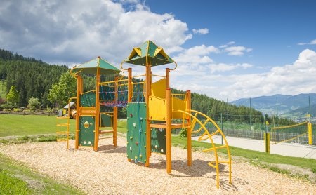 A colorful playground with a climbing frame and slide, surrounded by green grass and mountains.