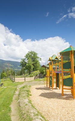 Ein Spielplatz mit Klettergerüst und Rutsche, umgeben von grüner Wiese und Bergen.