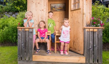 Vier Kinder stehen auf der Veranda eines Holzhauses und posieren für ein Foto.