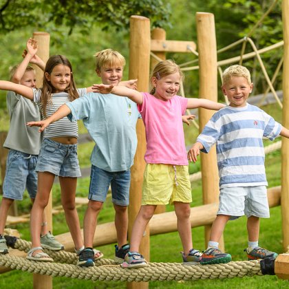 Kinder balancieren mit ausgestreckten Armen auf einem Seil im Outdoor-Spielplatz