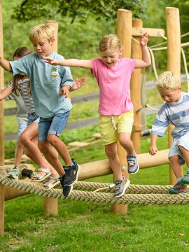 Children balancing on a thick rope on a wooden climbing structure outdoors