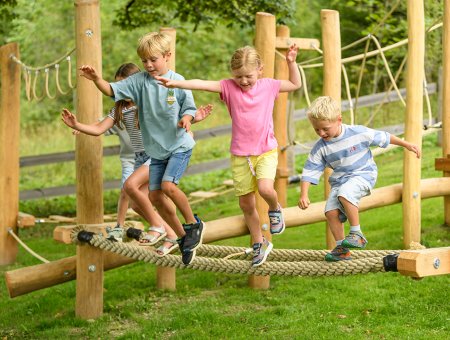Kinder balancieren auf einem dicken Seil im Freien auf einem Klettergerüst aus Holz