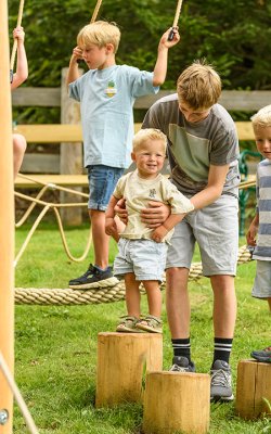Kinder spielen auf einem Klettergerüst im Freien mit Holzstämmen und Seilen