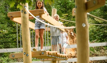 Kinder balancieren auf einer hölzernen Hängebrücke im Waldspielplatz