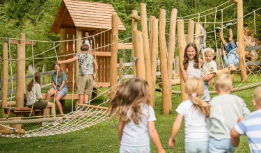 Kinder spielen auf einem Holzspielplatz mit Seilbrücken und Klettergerüsten im Freien