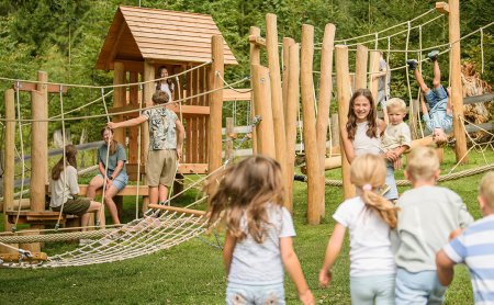 Children playing on a wooden playground with rope bridges and climbing structures outdoors