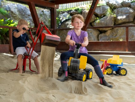 Zwei Kinder baggern mit Spielzeug im Sand unter dem Vordach
