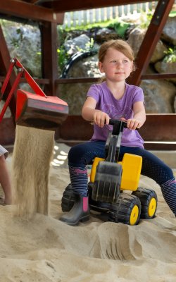 Zwei Kinder baggern mit Spielzeug im Sand unter dem Vordach