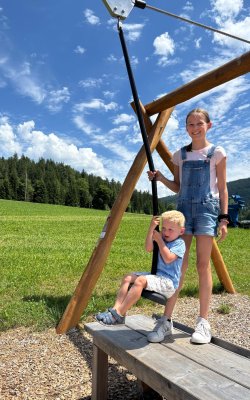 A girl and a boy are standing on the platform of a zip line.