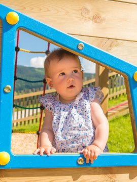 Ein kleines Mädchen schaut aus einem Fensterrahmen auf einem Spielplatz.